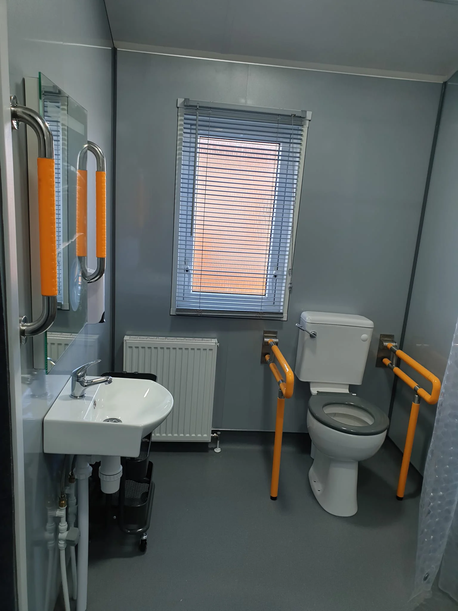 Accessible wet room with toilet and wheel under wash basin and handrails