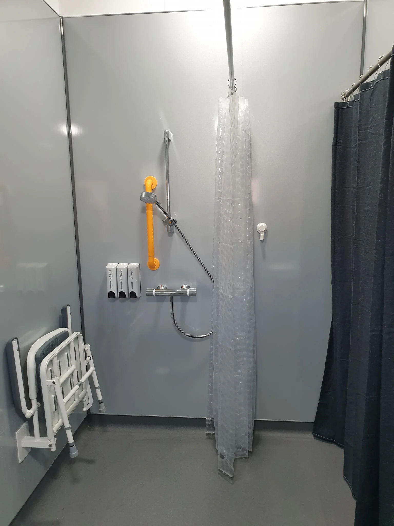 Accessible shower with handrails and wall mounted shower seat