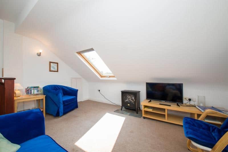 Bright cozy attic living room with blue sofas and TV