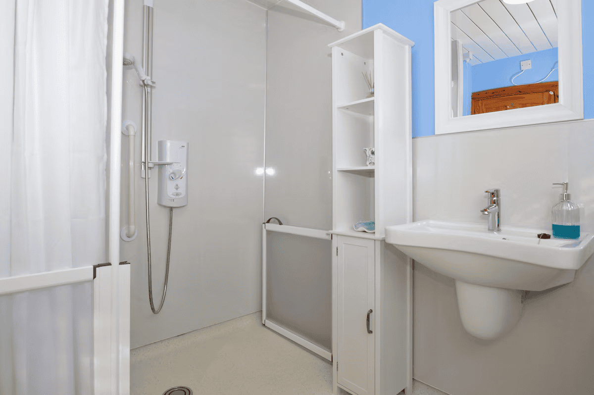 Clean white bathroom with shower, sink, and storage cabinet