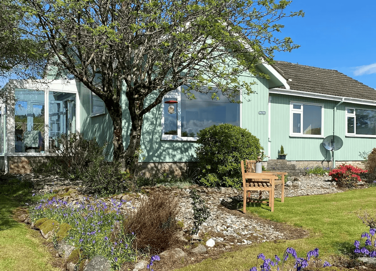 Charming green house with vibrant garden and wooden bench.