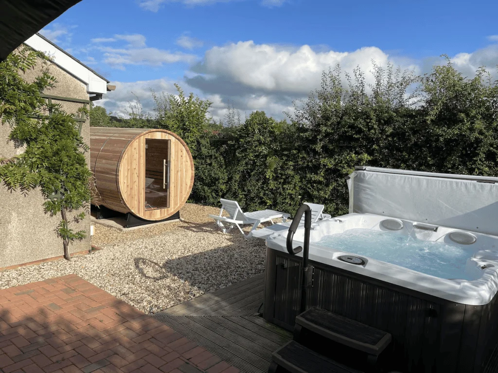 Outdoor hot tub and barrel sauna in lush backyard