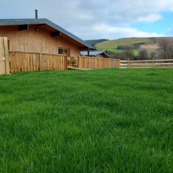 Wooden cabin with green lawn and distant hills