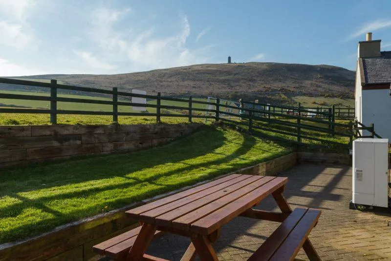 Picnic table on grass with fence and hill in distance
